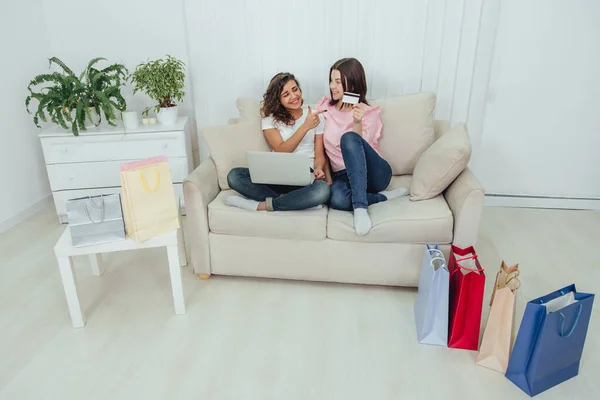 Two happy female friends using laptop for shopping online. One girl is holding credit card, another pointing her finger at it. — Stock Photo, Image