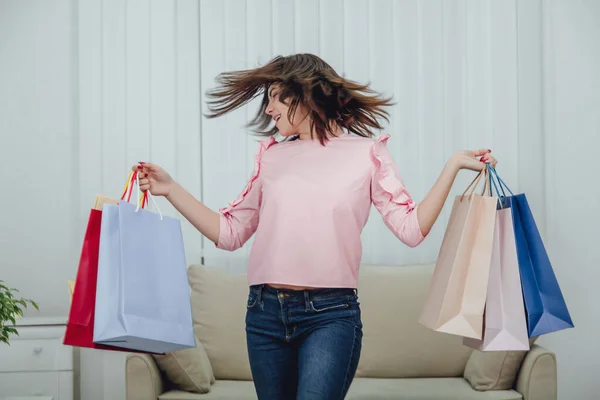 Pretty young girl is shaking her head making windy hair, standing with lot of shop bags in her hands. — Stock Photo, Image