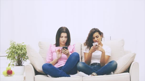 Belle giovani ragazze caucasiche afro-americane e brune eccentriche sono sedute sul divano in posizione foto, con il telefono in mano, messaggistica . — Video Stock