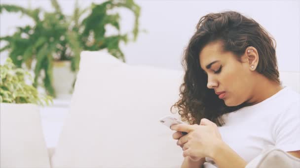 Heerlijk kinky Afrikaans-Amerikaans meisje zit op de bank met telefoon in haar handen en ziet er ziek en moe uit. Ze heeft hoofdpijn en massages haar slapen. — Stockvideo