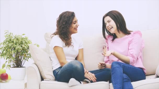 Caucasian brunette girl is bending her fingers, counting some reasons or facts. Two girl friends are talking sitting on the sofa in warm home environment. — Stock Video