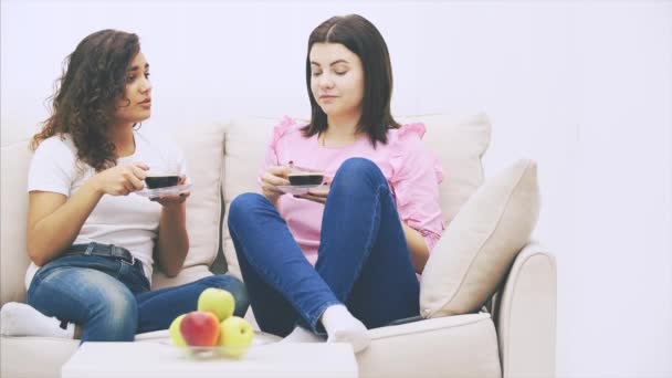 Zwei Freundinnen unterhalten sich auf dem Sofa in warmer häuslicher Umgebung und trinken Kaffee. Teller mit Äpfeln auf dem Tisch im verschwommenen Vordergrund. — Stockvideo