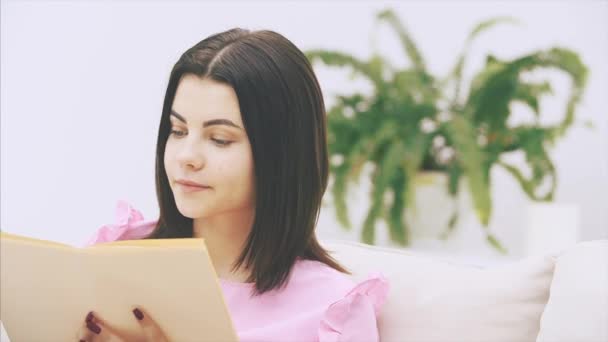 Zvídavá mladá žena sedí na pohovce, listuje stránkami knihy, vypadá ohromeně a vzrušeně. — Stock video