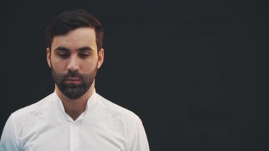 Yakışıklı genç adam aşağı bakıyor, sonra kameraya bakıyor, ellerini kavuşturuyor..