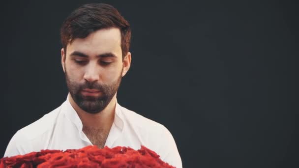 Bel homme debout avec un grand bouquet de roses rouges, l'étendant à la caméra, souriant, hochant la tête et levant les sourcils . — Video