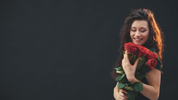 Милая кудрявая брюнетка, стоящая, пахнущая красными розами. Курьер идет по фону с буфером . — стоковое видео