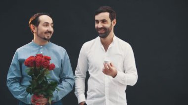 Güller ve yüzüklerle yan yana duran, gülümseyen, mutlu görünen iki adam. Tipik yönelim.