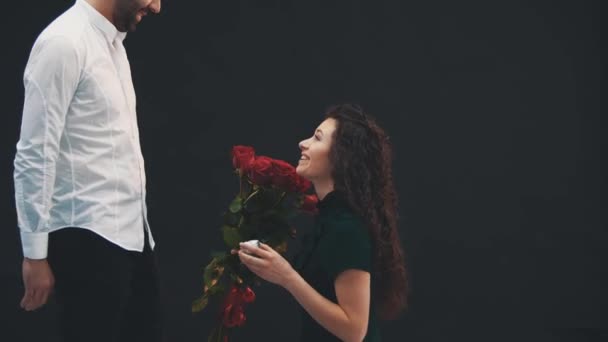 Mujer rizada divertida está de pie sobre una rodilla con anillo y rosas en sus manos, haciendo propuesta de su hombre. Dice que sí. . — Vídeos de Stock