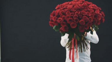 Genç adam ayakta, kırmızı güllerin arkasına saklanıyor, sonra korkmuş yüzünü gösteriyor, ağzını ve gözlerini kocaman açıyor..