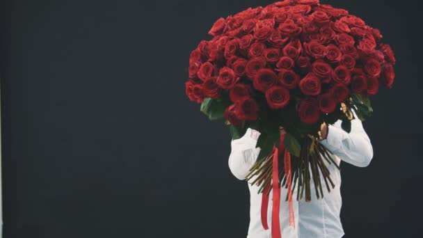 Młody mężczyzna stoi,, chowa się za bukietem czerwonych róż, a następnie pokazuje jej przerażoną twarz, szeroko otwarte usta i oczy. — Wideo stockowe