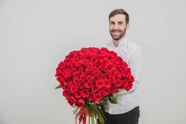 Adam heyecanlı görünüyor, karısı için bir demet narin çiçekle dikiliyor, beyaz arka planda..
