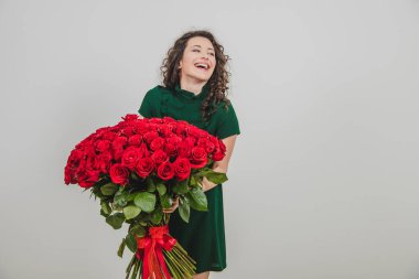 Uzun dalgalı saçlı neşeli genç bayan beyaz arka planda izole edilmiş kadınlar gününde bir buket kırmızı gül almak için heyecanlanıyor..