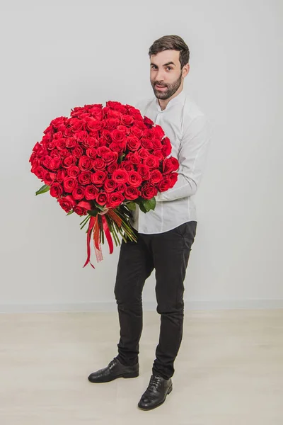 Κομψό γενειοφόρος άνδρας κρατώντας ένα μπουκέτο κόκκινα τριαντάφυλλα για την ημέρα του Αγίου Βαλεντίνου, απομονώνονται σε λευκό φόντο. — Φωτογραφία Αρχείου