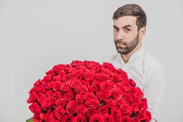 Ritratto ravvicinato di elegante uomo barbuto con in mano un mazzo di rose rosse per San Valentino, isolato su sfondo bianco . — Foto Stock