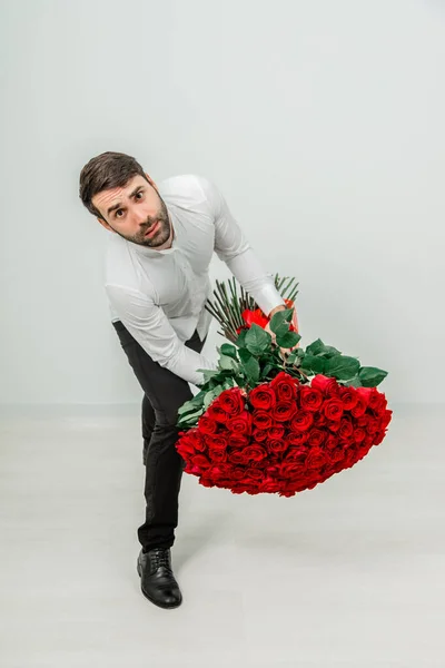 Giovane uomo con rose pesanti bouquet, appoggiato alla macchina fotografica, accigliato, guardando infelice . — Foto Stock