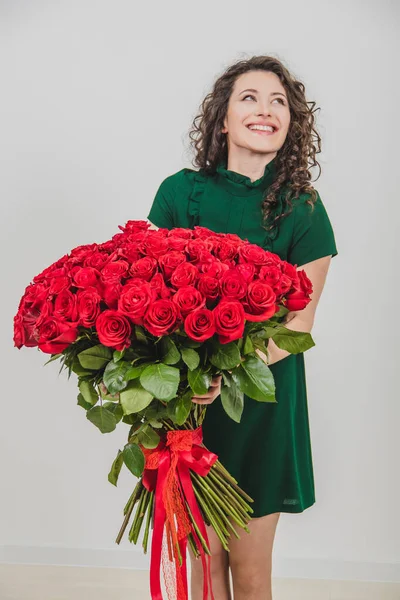 Cheerful young lady with long wavy hair being excited to get bouquet of red roses on Womens day isolated over white background.