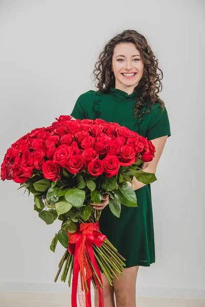 Beautiful young woman with rose bouquet, looking delighted and loved, over white background.