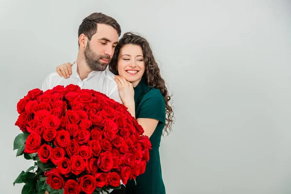 Heureux couple élégant est câlin et souriant, sur fond blanc. L'homme tient des roses . — Photo