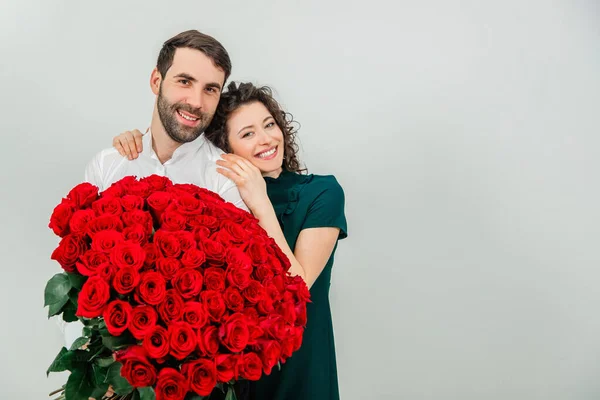 Conceito de amor verdadeiro. Casal afetuoso de pé juntos, brilhando com felicidade, segurando lindo monte de rosas . — Fotografia de Stock