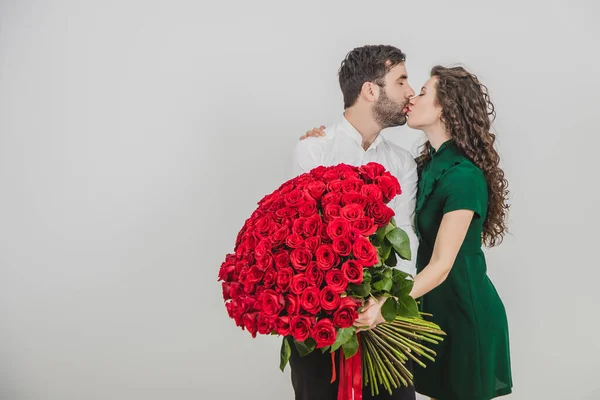 Stilig man och hans kvinna står över vit backgroud med rosor i händerna, kyssas efter att hon säger ja till hans förslag. — Stockfoto