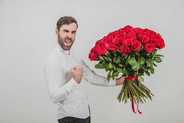 Bell'uomo in piedi con un grande mazzo di rose rosse legate a strisce, masticando il pugno, come un macho, perché la sua ragazza ha detto che ha accettato di sposarlo . — Foto Stock