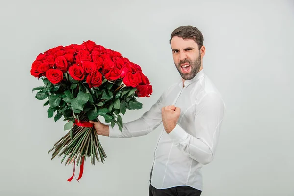 Bell'uomo in piedi con un grande mazzo di rose rosse legate a strisce, masticando il pugno, come un macho, perché la sua ragazza ha detto che ha accettato di sposarlo . — Foto Stock