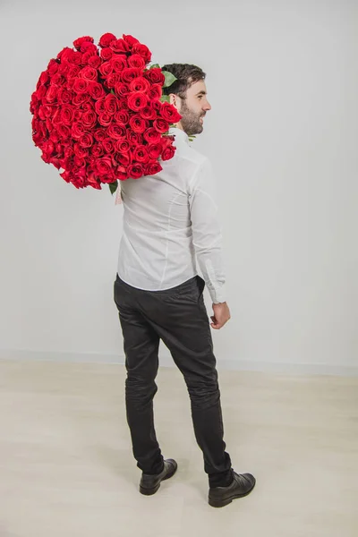 Ritratto di uomo sicuro di sé in abiti formali, in piedi di nuovo alla macchina fotografica, portando un mazzo di rose rosse sulla spalla . — Foto Stock