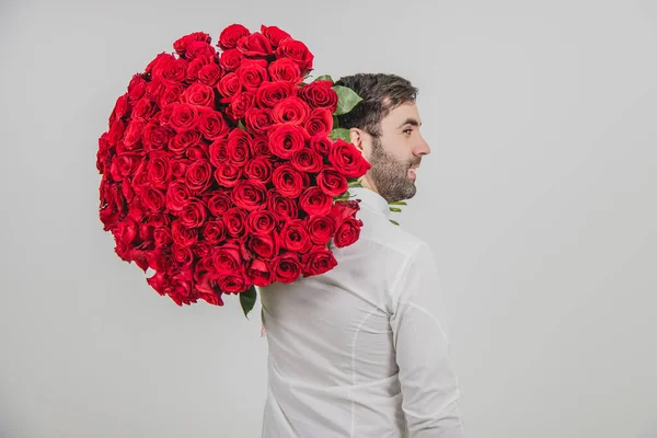 Ritratto di uomo sicuro di sé in abiti formali, in piedi di nuovo alla macchina fotografica, portando un mazzo di rose rosse sulla spalla . — Foto Stock