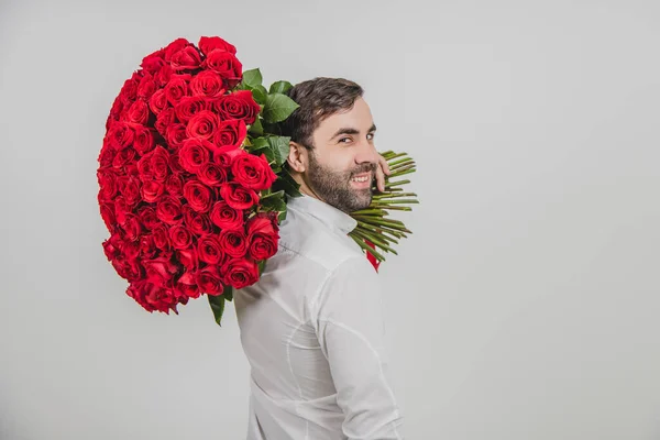 Πορτρέτο του άνδρα αυτοπεποίθηση σε επίσημα ρούχα, στέκεται πίσω στην κάμερα, carring ένα μπουκέτο κόκκινα τριαντάφυλλα στον ώμο του. — Φωτογραφία Αρχείου