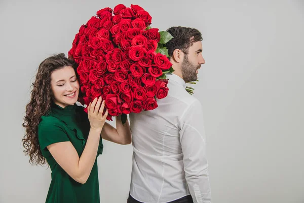 Jeune homme et femme romantique posant avec un bouquet de roses rouges sur fond blanc . — Photo