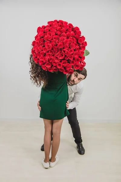 一对有趣的夫妇在白色背景上与一束红玫瑰开玩笑和鬼混. — 图库照片