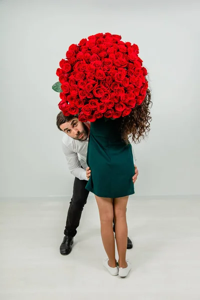 Coppia divertente scherzare e ingannare con mazzo di rose rosse su sfondo bianco . — Foto Stock