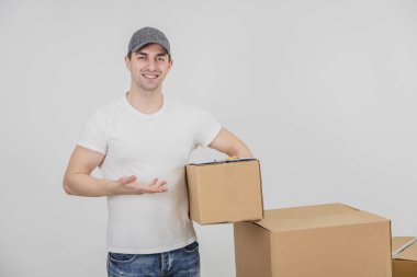 Genç teslimatçı ayakta, elinde karton bir paket, parmağıyla işaret ediyor, gülümsüyor..