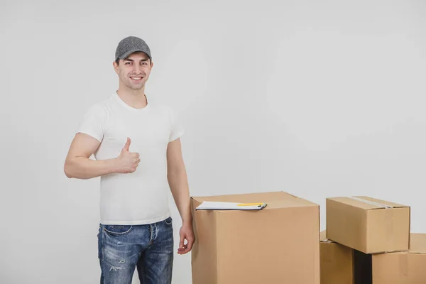 Lächelnder junger Zusteller, der neben einem Stapel Pappschachteln steht und den Daumen hebt. — Stockfoto