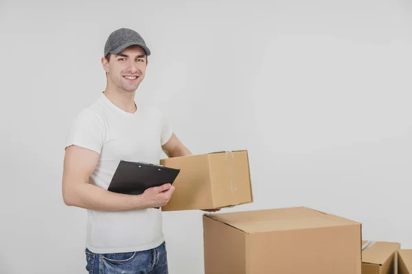 Schöner junger Zusteller, der mit Klemmbrett und Karton in der Hand in die Kamera blickt. — Stockfoto