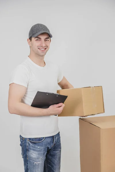 Schöner junger Zusteller, der mit Klemmbrett und Karton in der Hand in die Kamera blickt. — Stockfoto