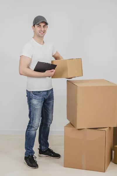 Schöner junger Zusteller, der mit Klemmbrett und Karton in der Hand in die Kamera blickt. — Stockfoto