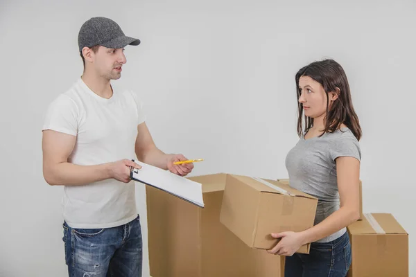 Uma jovem a mudar-se para um lugar novo. Entrega cara transportou todas as caixas de papelão em seu novo apartamento e está esperando por sua assinatura . — Fotografia de Stock