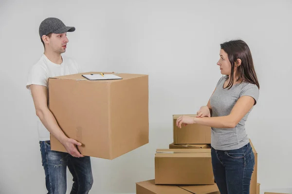 O entregador transportou todas as caixas de papelão para o novo apartamento feminino, mas tarde demais e a mulher está irritada por causa disso. Courier está olhando para ela com expressão facial inocente . — Fotografia de Stock