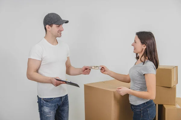 Jovem está pagando um cara de entrega para o transporte de caixas de papelão em novo apartamento . — Fotografia de Stock