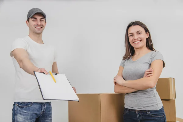 O homem de entrega feliz transportou caixas no novo apartamento da jovem encantadora e está mostrando a declaração assinada, sorrindo. Ambos estão felizes pela cooperação . — Fotografia de Stock