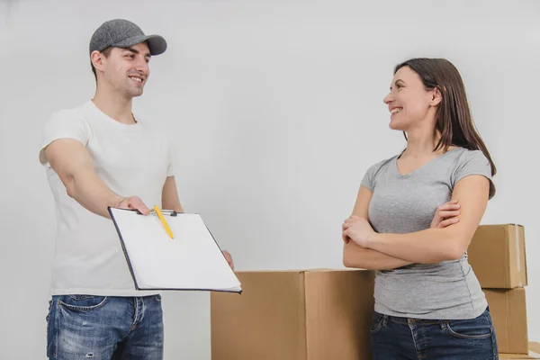 O homem de entrega feliz transportou caixas no novo apartamento da jovem encantadora e está mostrando a declaração assinada, sorrindo. Ambos estão felizes pela cooperação . — Fotografia de Stock