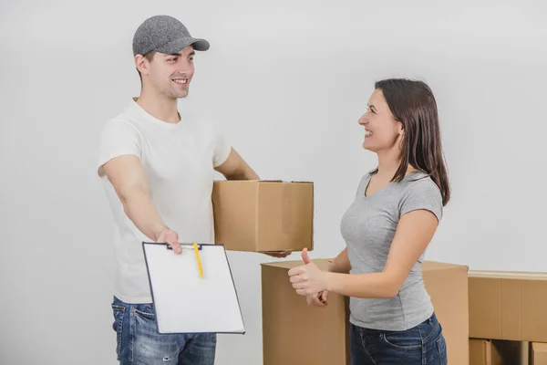 O homem de entrega feliz transportou caixas no novo apartamento da jovem encantadora e está mostrando a declaração assinada, sorrindo. Ambos estão felizes pela cooperação . — Fotografia de Stock