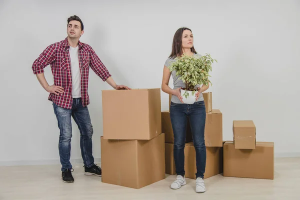 O jovem casal feliz mudou-se para um novo apartamento. Mulher com vaso nas mãos, e homem com sua mão akimbo estão olhando ao redor, pensando como fornecer nova casa . — Fotografia de Stock