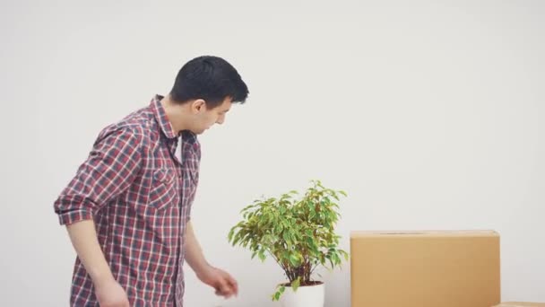 Handsome jongeman bracht bloempot in zijn nieuwe appartementen, staande handen gevouwen, dan wijzen naar de copyspace aan de zijkant. — Stockvideo