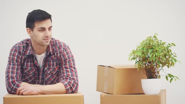 Jeune homme debout dans ses nouveaux appartements, appuyé sur la pile de boîtes en carton, souriant, prenant des clés de poche à la nouvelle maison . — Video