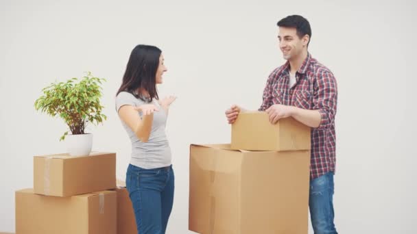 Egy pár egy új lakásban. A nő áll, mosolyog. A fiatalember teljesen kimerült. Már nem tud nehéz dobozokat cipelni.. — Stock videók