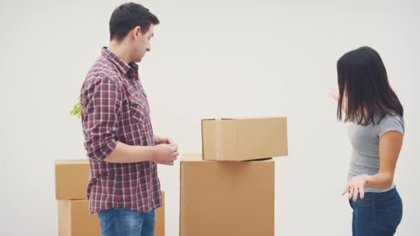 La pareja se está mudando a un piso nuevo. Tienen una pelea, porque no saben dónde poner todas esas cajas de cartón grandes. La mujer está lista para tirarle la caja al hombre . — Vídeos de Stock