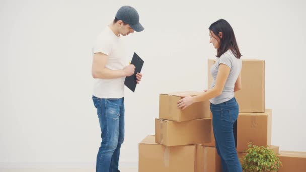 Genç bir kadın yeni bir yere taşınıyor. Karton kutuları yeni daireye taşıması için bir kurye çağırmış.. — Stok video