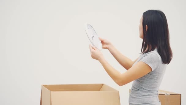 Mujer entusiasta desempacando cajas de cartón, sacando el reloj blanco, pensando dónde colgarlo. Mensajero apareciendo con un regalo para ella, pidiendo poner una firma . — Vídeo de stock